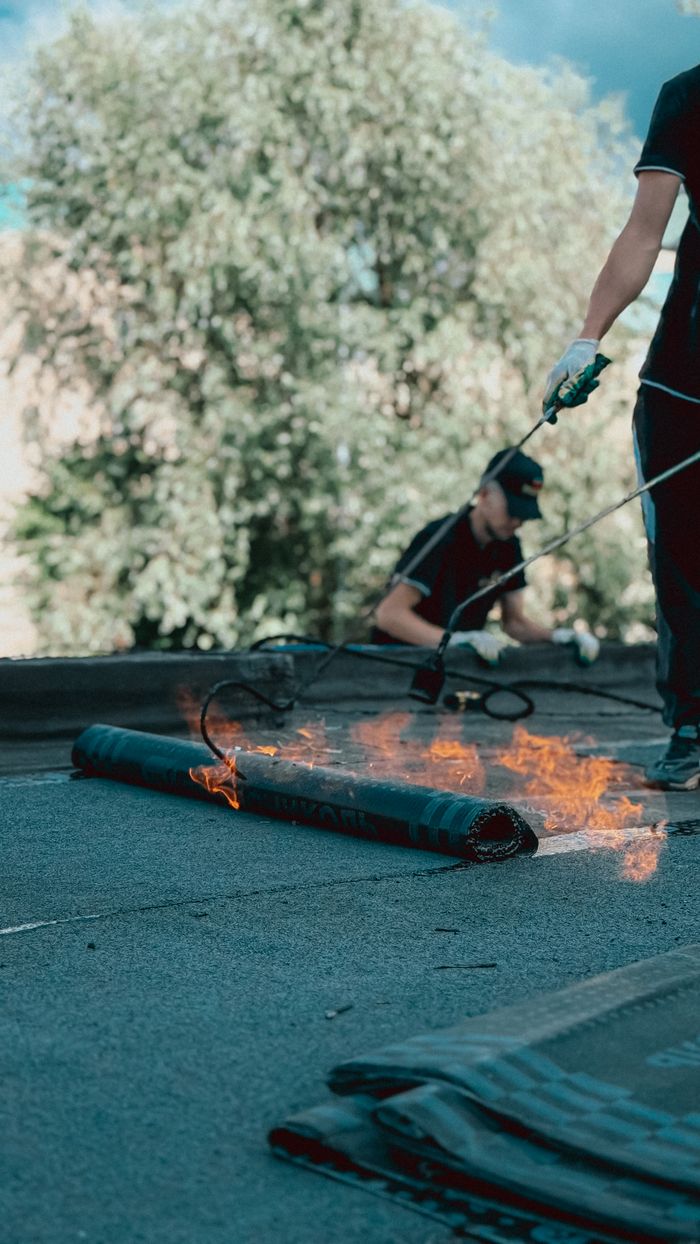 Crafting Captivating Headlines: Your awesome post title goes here Roofers applying torch down rubber membrane for waterproofing. Outdoor construction scene highlighting skilled labor.