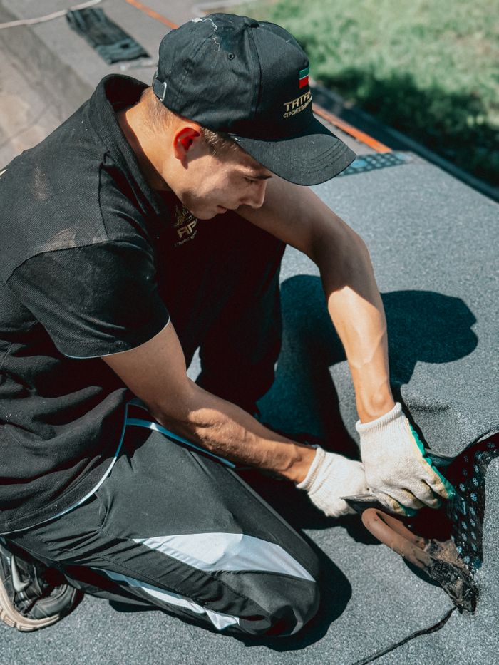 A professional roofer installs a black waterproof membrane on a rooftop during daytime.